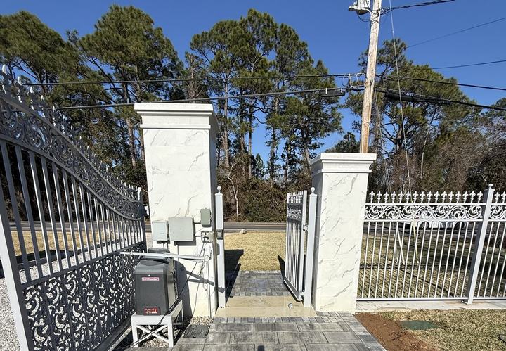 Ornamental metal gated entrance with white columns and paver landing